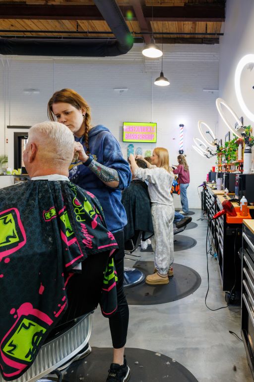 Women cut customers' hair at Bareknuckles Barber Shop